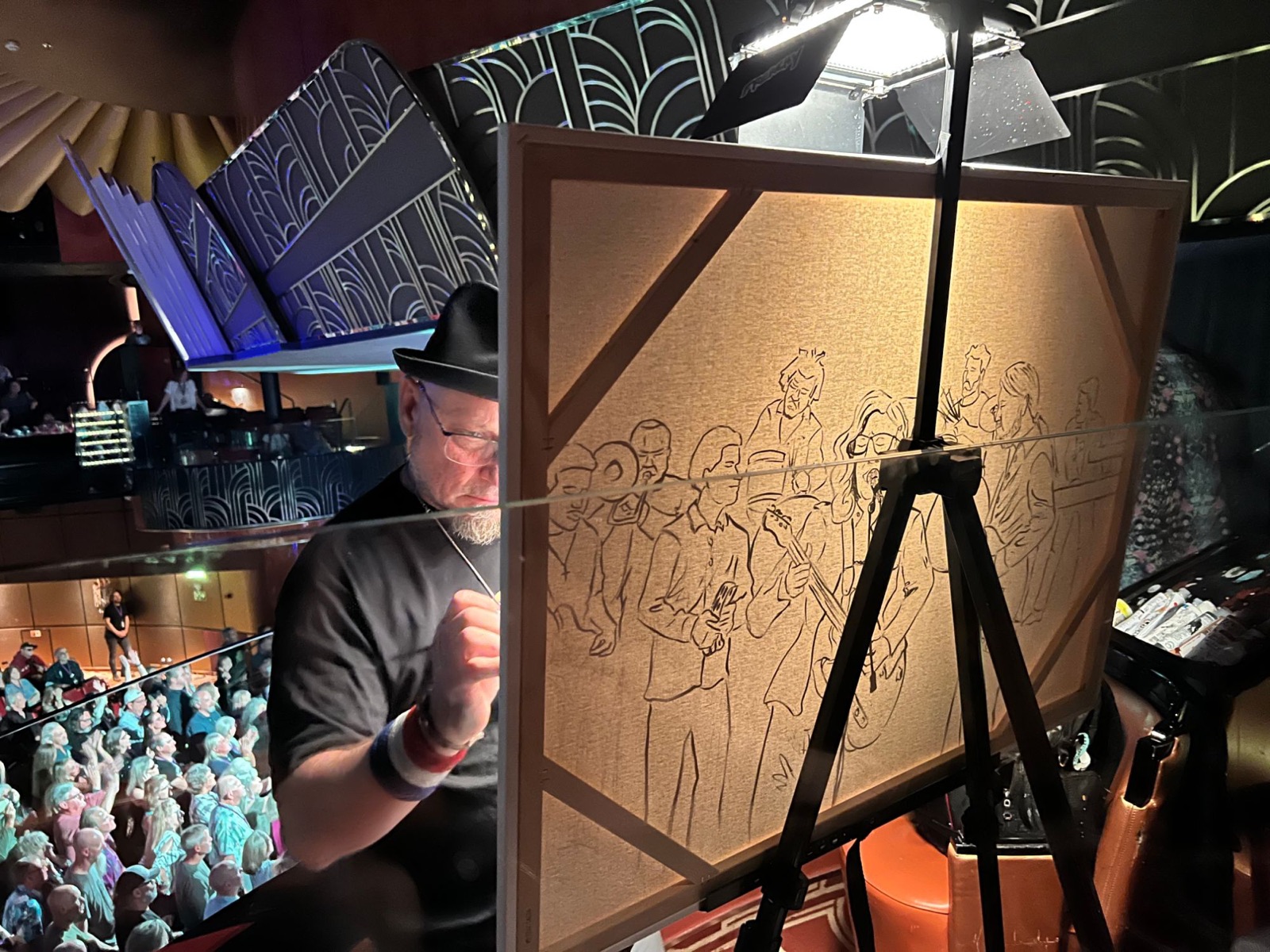 Frenchy inking a band on canvas from the balcony during a Big Easy Cruise show, the crowd below